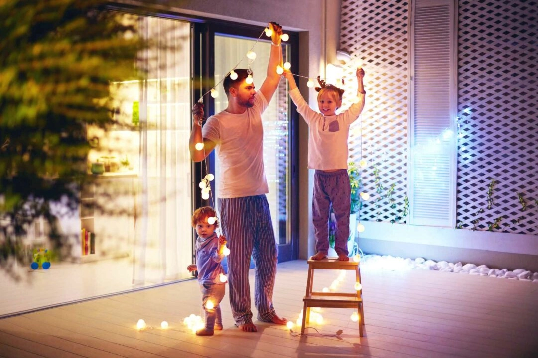 Un père et ses enfants installent une guirlande lumineuse dans la cour d'une maison