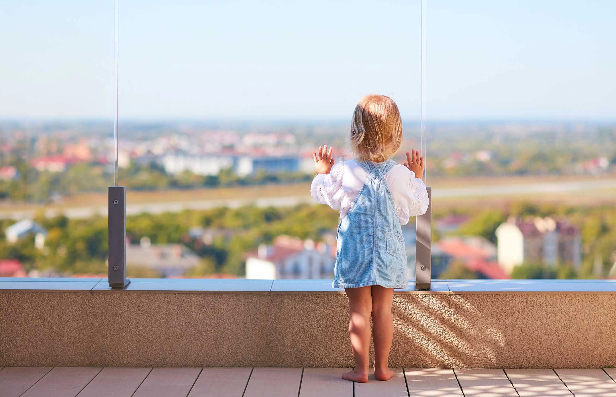 Une jeune enfant regarde le paysage sur un terrasse protégée par un garde corps