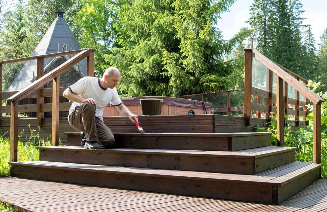 Un homme entretien un escalier en bois menant à un jacuzzi dans un jardin paysager