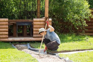 Un artisan paysagiste étale du gravier sur un film géotxtile dans un jardin