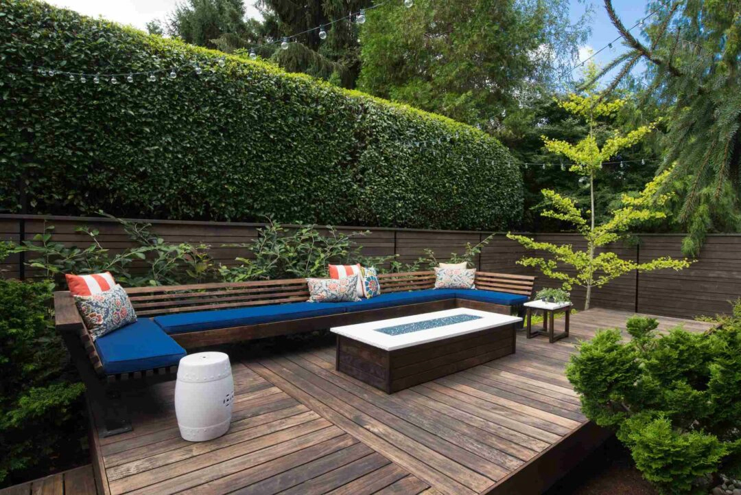 Un grand salon de jardin sur une terrasse en bois protégée du vent par une grande haie végétale