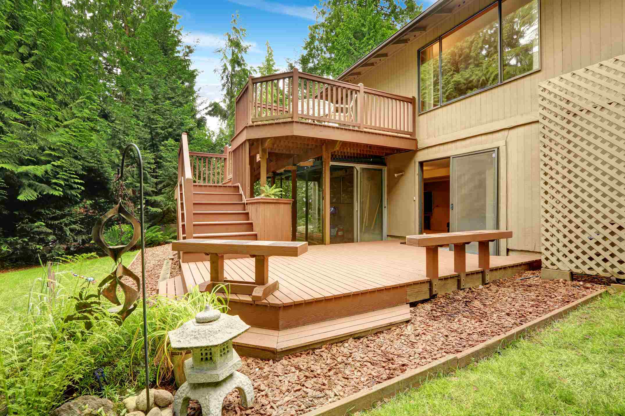 Une terrasse supendue et sa belle maison en bois dans un jardin paysager