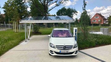 Une voiture électrique en cours de cahrgement près d'un carport équipé de panneaux solaires