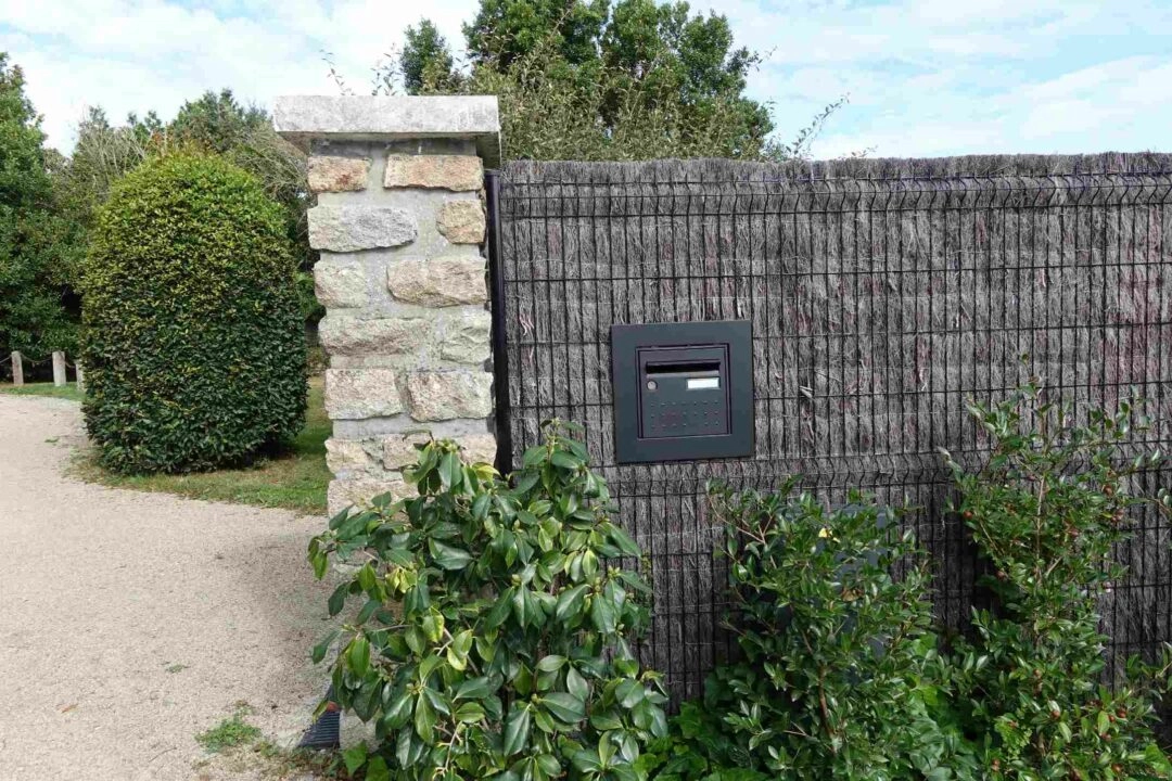 L'entrée d'une propriété avec sa clôture grillagée et un dispositif occultant